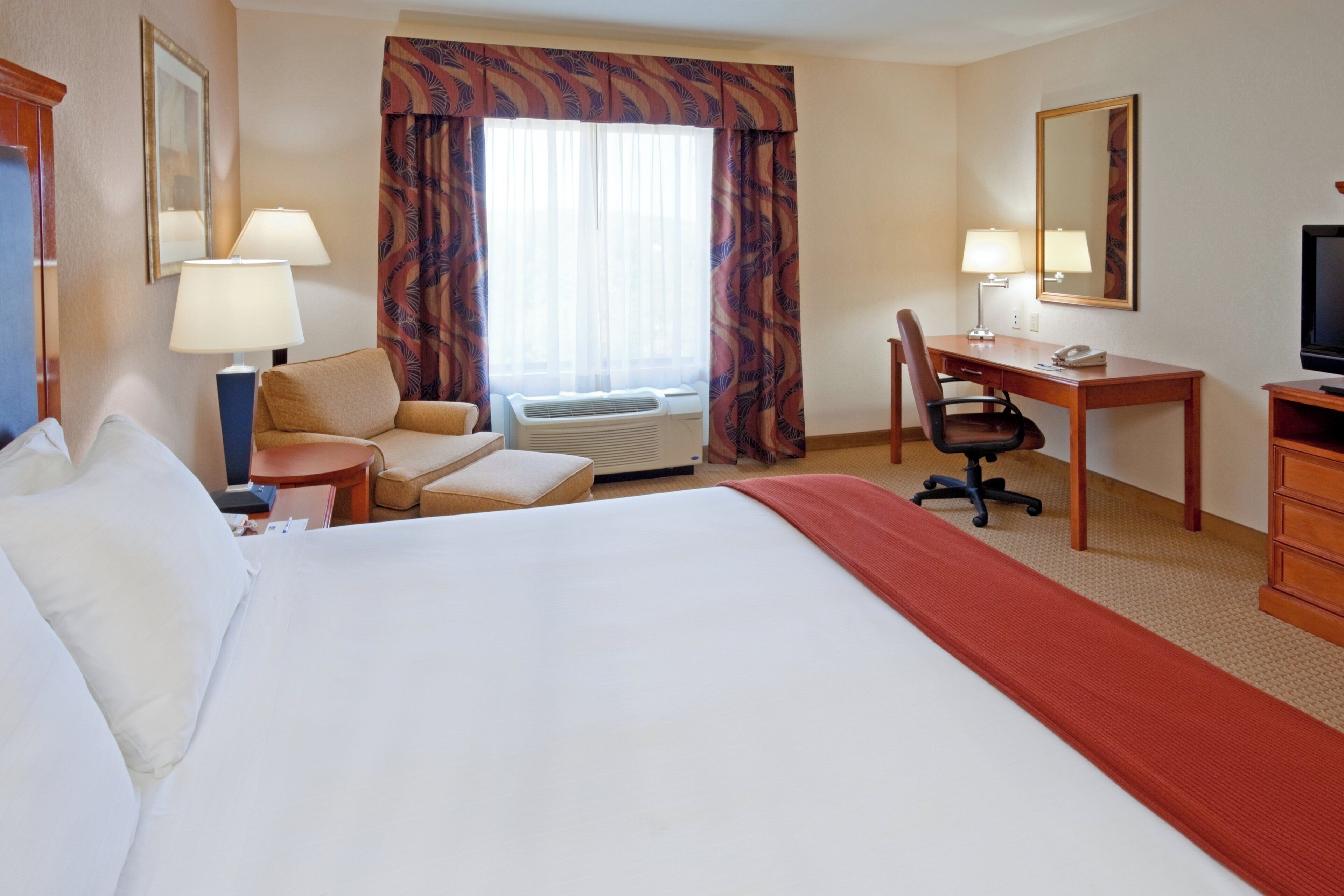 A hotel room with a bed, a desk, a chair, a television, and a window with curtains.