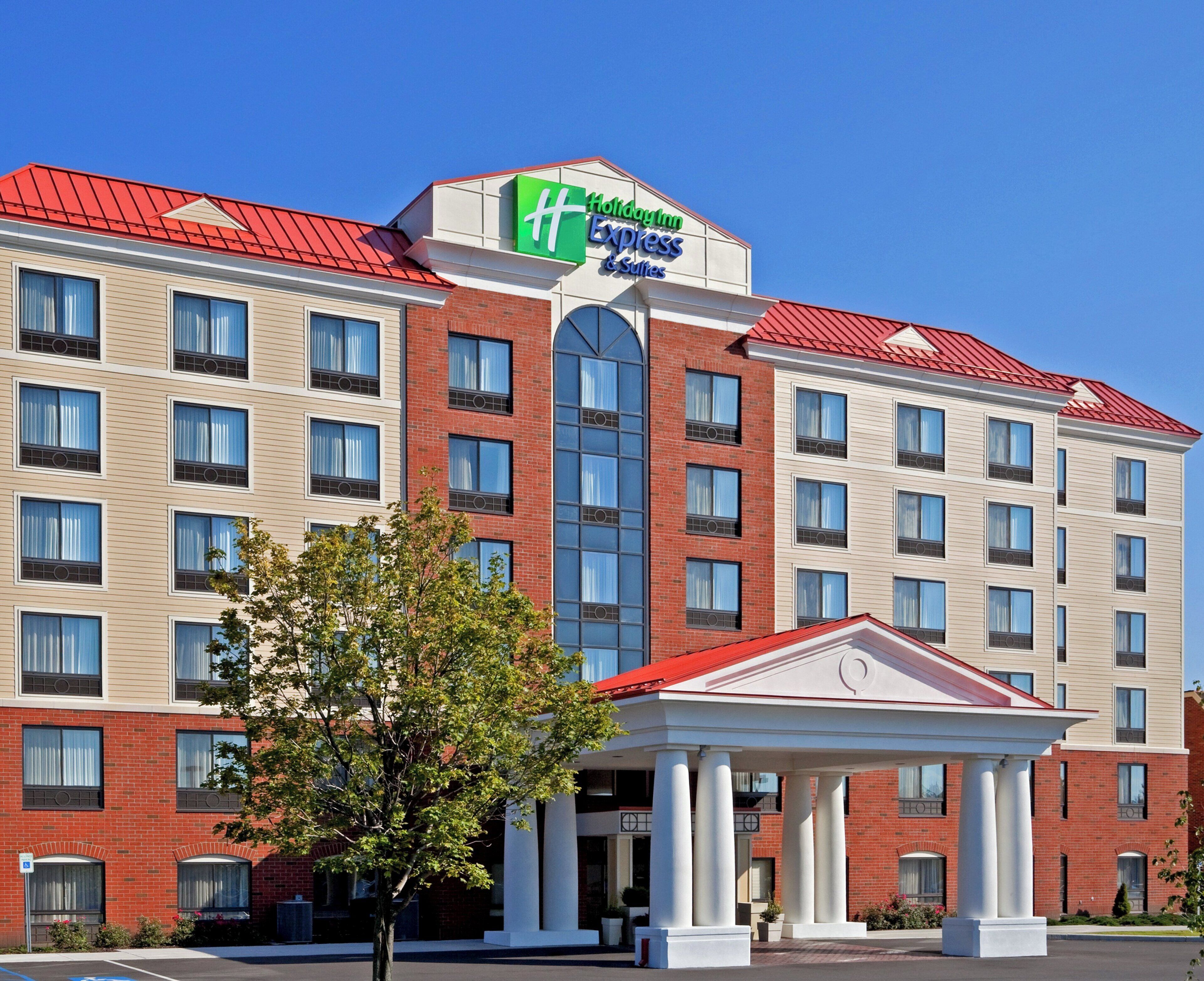 A Holiday Inn Express & Suites hotel with a red roof, multiple windows, and a central entrance with columns.