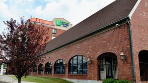 A brick building with a Holiday Inn Express sign, large arched windows, and a well-maintained lawn. - Holiday Inn Express & Suites Albany Airport Area - Latham by IHG (Latham)