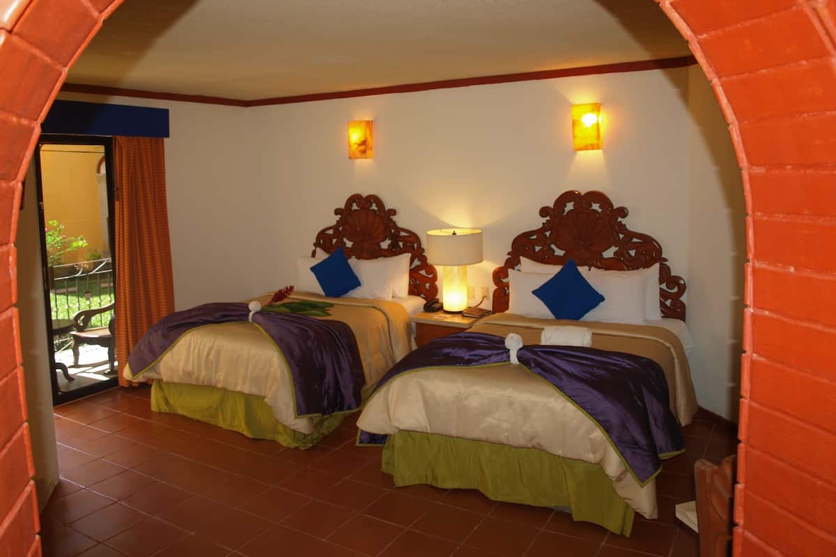 A hotel room with two beds, a balcony, and a brick archway.