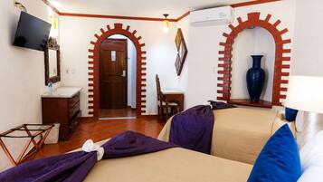 Habitación de hotel con cama, escritorio, silla, televisión, espejo, armario y un arco de entrada.