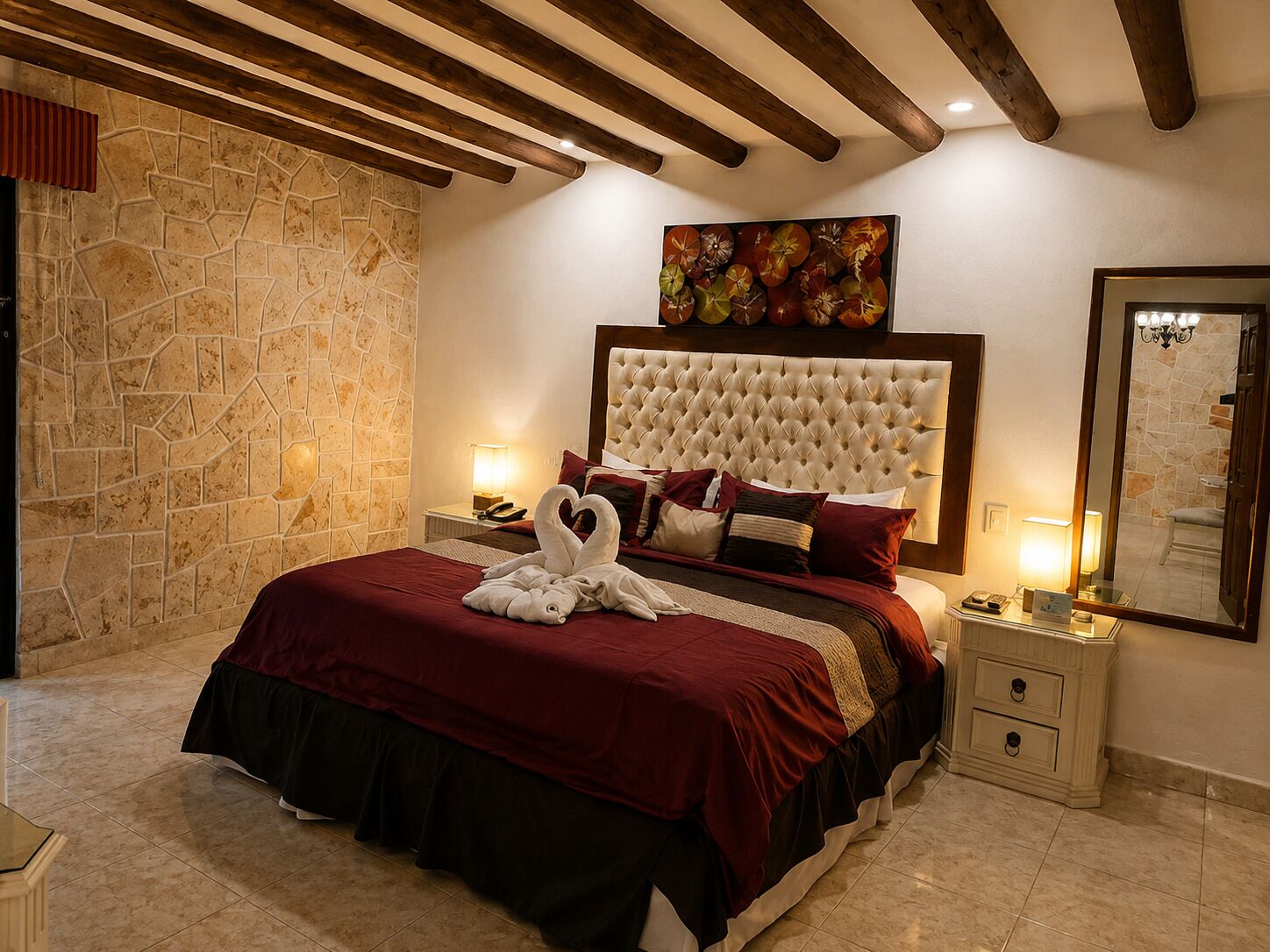 Quarto de hotel com parede de pedra, uma cama grande com cabeceira estofada e um quadro sobre a cama.