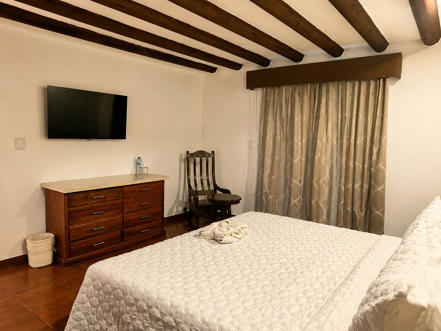 A bedroom with a bed, a dresser, a chair, a television, and a window with curtains.