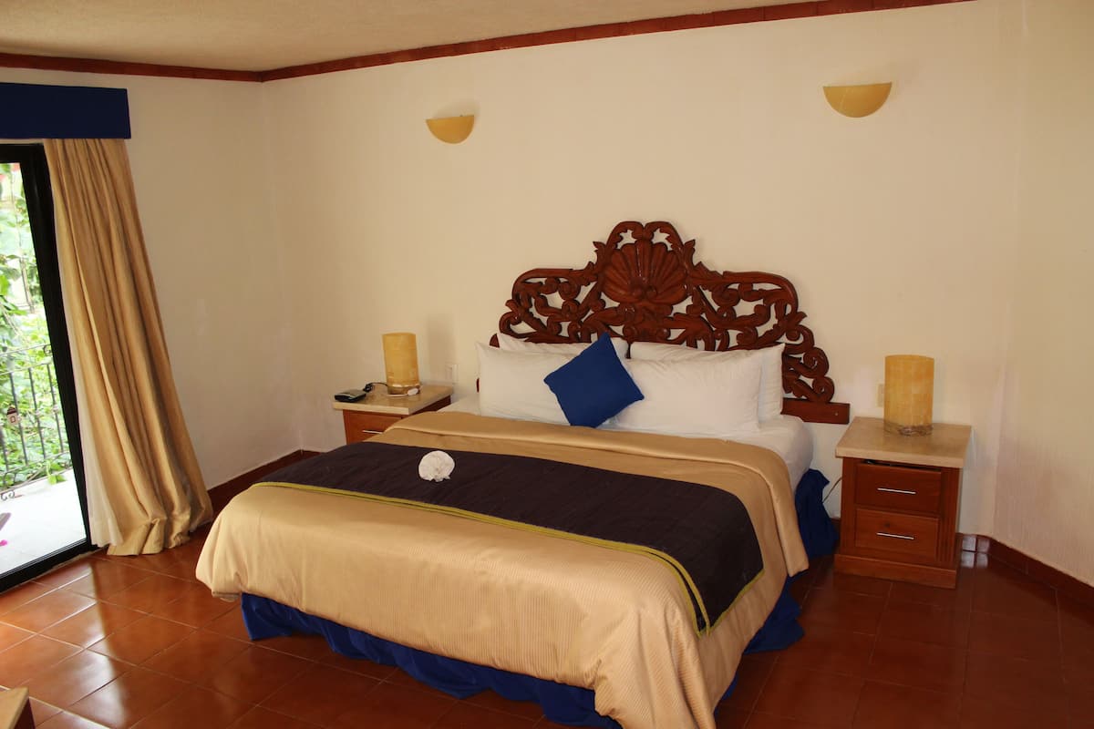 A bedroom with a large bed, wooden headboard, two bedside tables with lamps, and a view through a glass door.