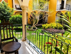 A courtyard with a wooden bench, a metal railing, and various plants.