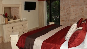 A bedroom with a large bed, a dresser, a television, and a stone wall.