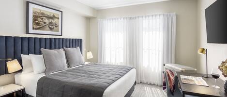A modern hotel room with a large bed, a desk, and a television.