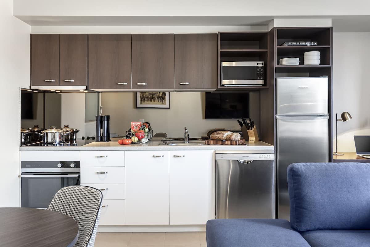 Una cocina moderna con electrodomésticos de acero inoxidable, armarios blancos y un comedor con sofá azul.