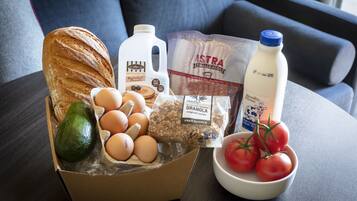 A box of groceries including bread, eggs, tomatoes, milk, and granola on a table.