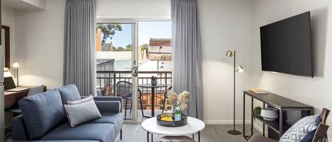 A modern living room with a sofa, coffee table, and ottoman, a small table with a tray, a TV mounted on the wall, and a balcony with a view.