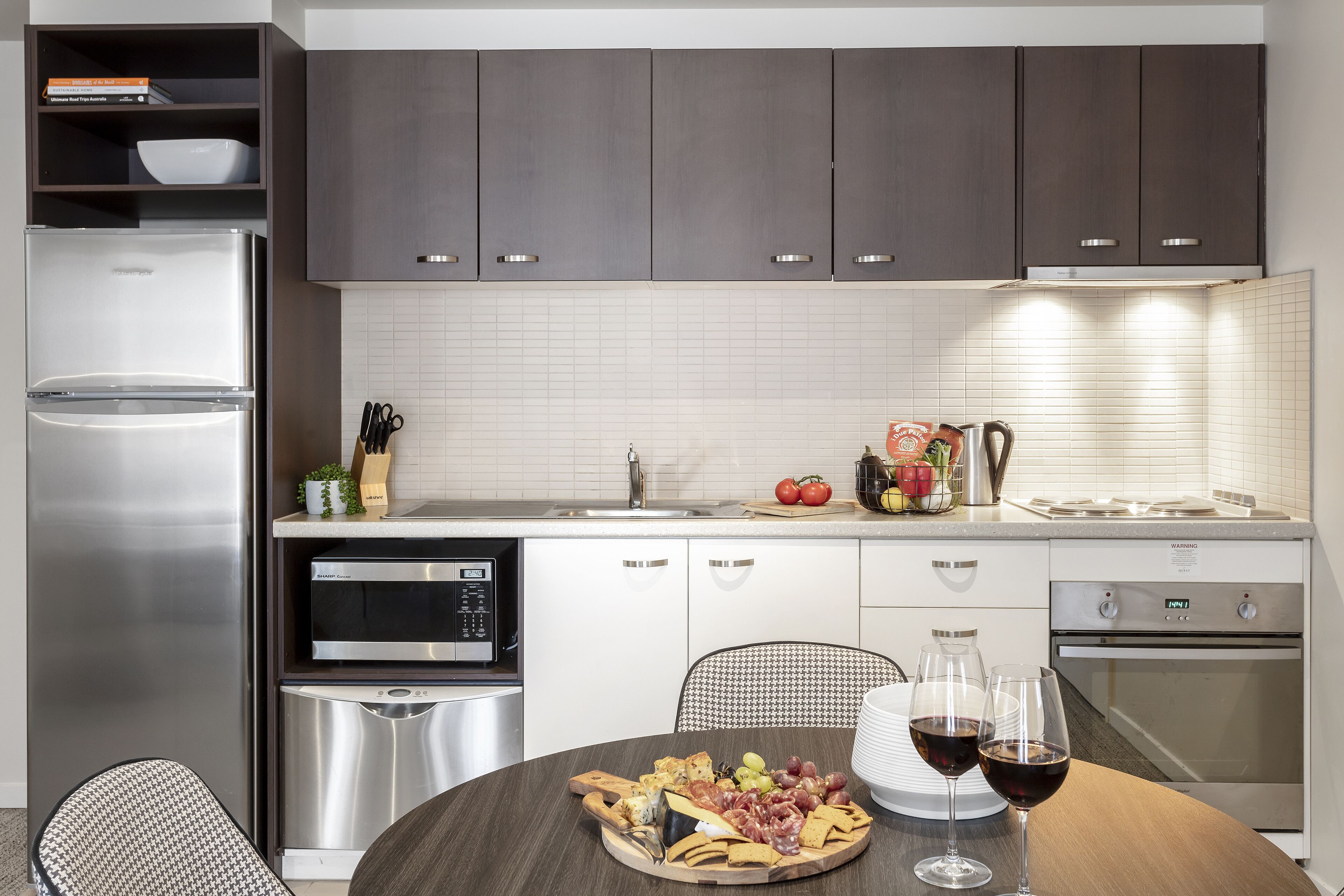 Una cocina moderna con armarios oscuros, electrodomésticos de acero inoxidable y un comedor con una mesa dispuesta para una comida.