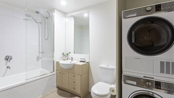 A modern bathroom with a glass-enclosed shower, a sink, a toilet, and a stacked washer and dryer.