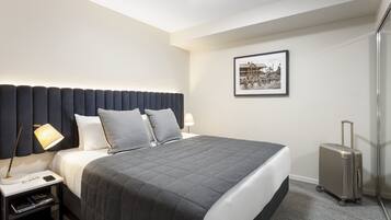 A hotel room with a large bed, a nightstand with a lamp, a suitcase, and a framed picture on the wall.