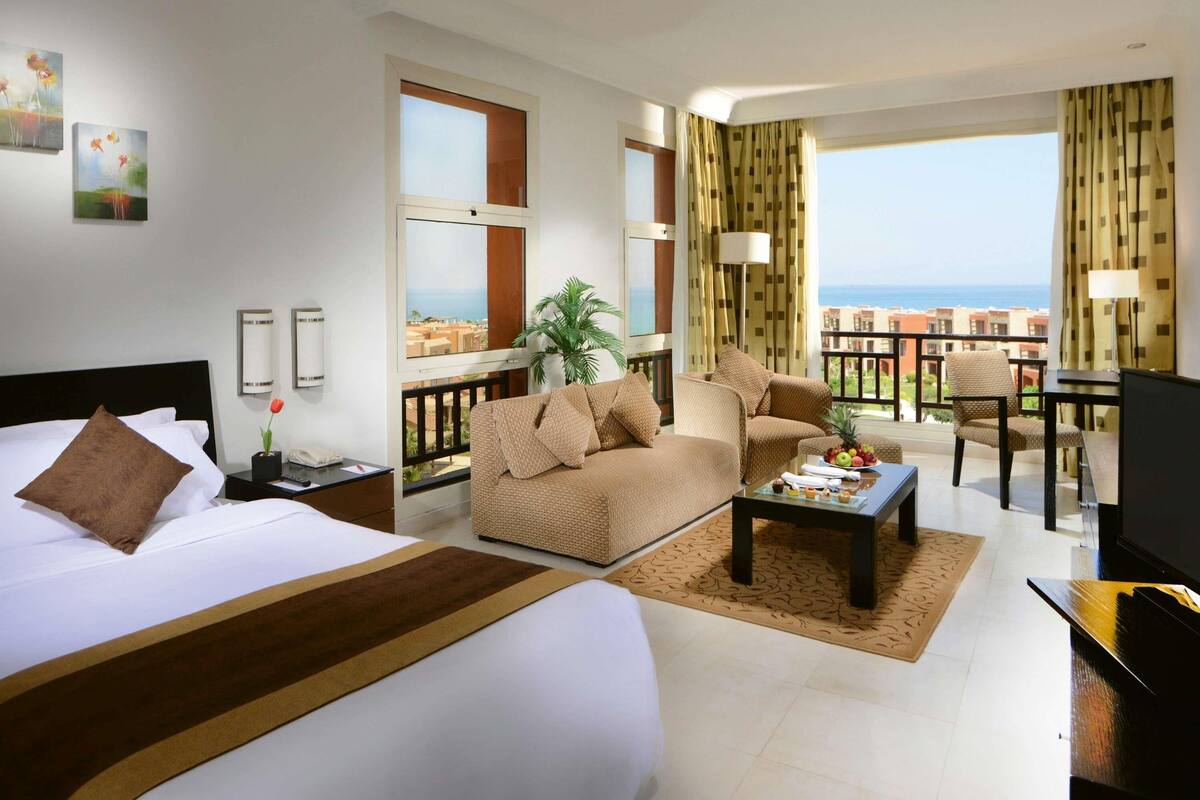 Ein Hotelzimmer mit Bett, einer Couch, einem Couchtisch, einem Fernseher und einem Balkon mit Meerblick.