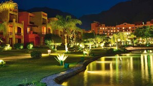 A hotel with multiple buildings, a well-lit garden, and a calm water feature. - Mövenpick Resort El Sokhna (Ataqah)