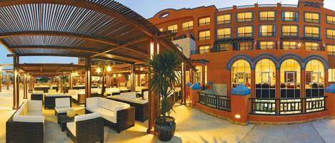 A hotel with outdoor seating, a covered patio, and a building with multiple windows and balconies.