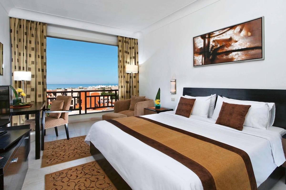A hotel room with a large bed, a desk, and a view of the city.