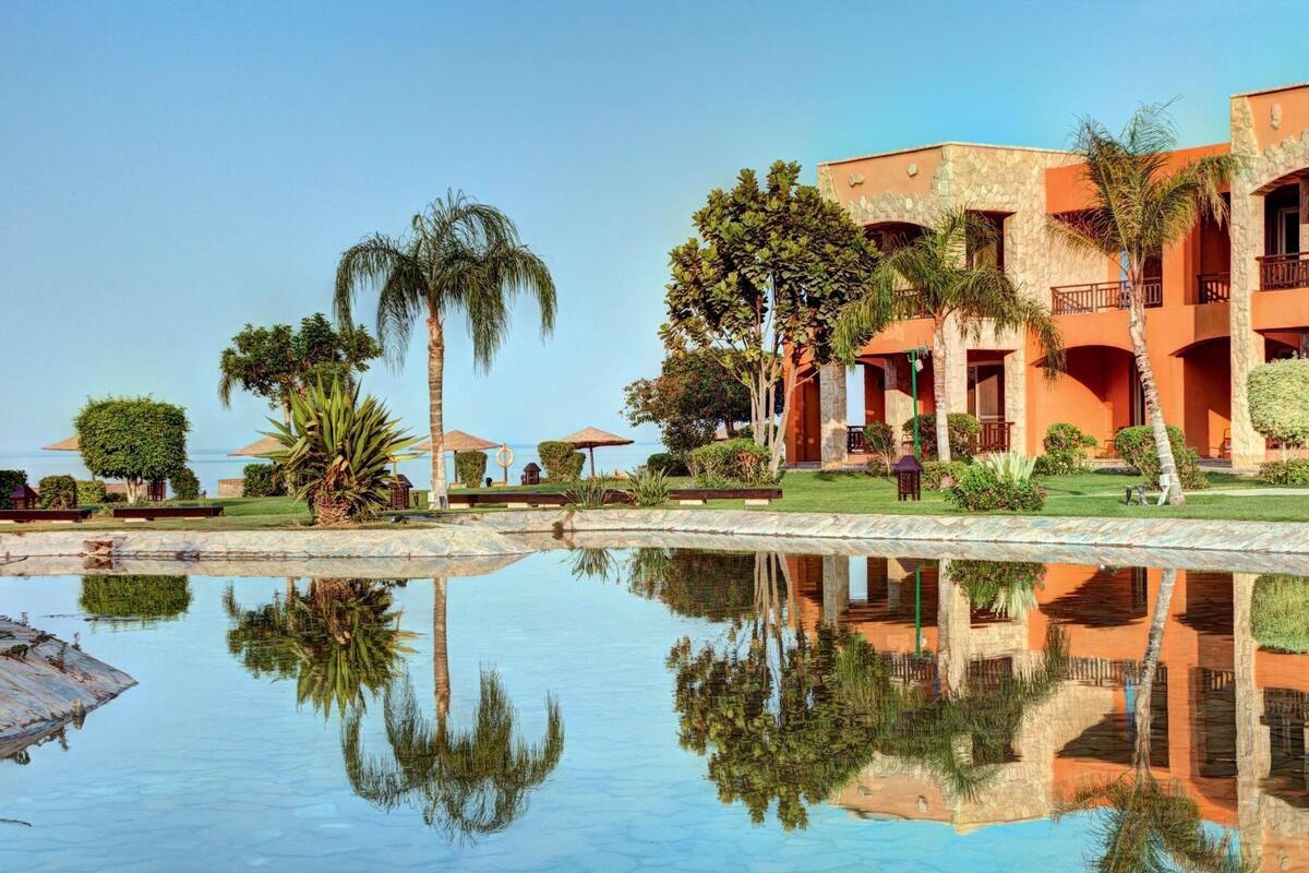 Ein Resort mit Pool, in dem Palmen sich spiegeln, und einem Gebäude mit Balkonen.