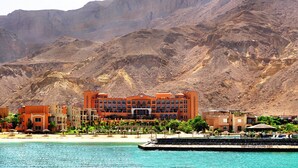 A hotel with multiple buildings, a beach, and a mountainous backdrop. - Mövenpick Resort El Sokhna (Ataqah)