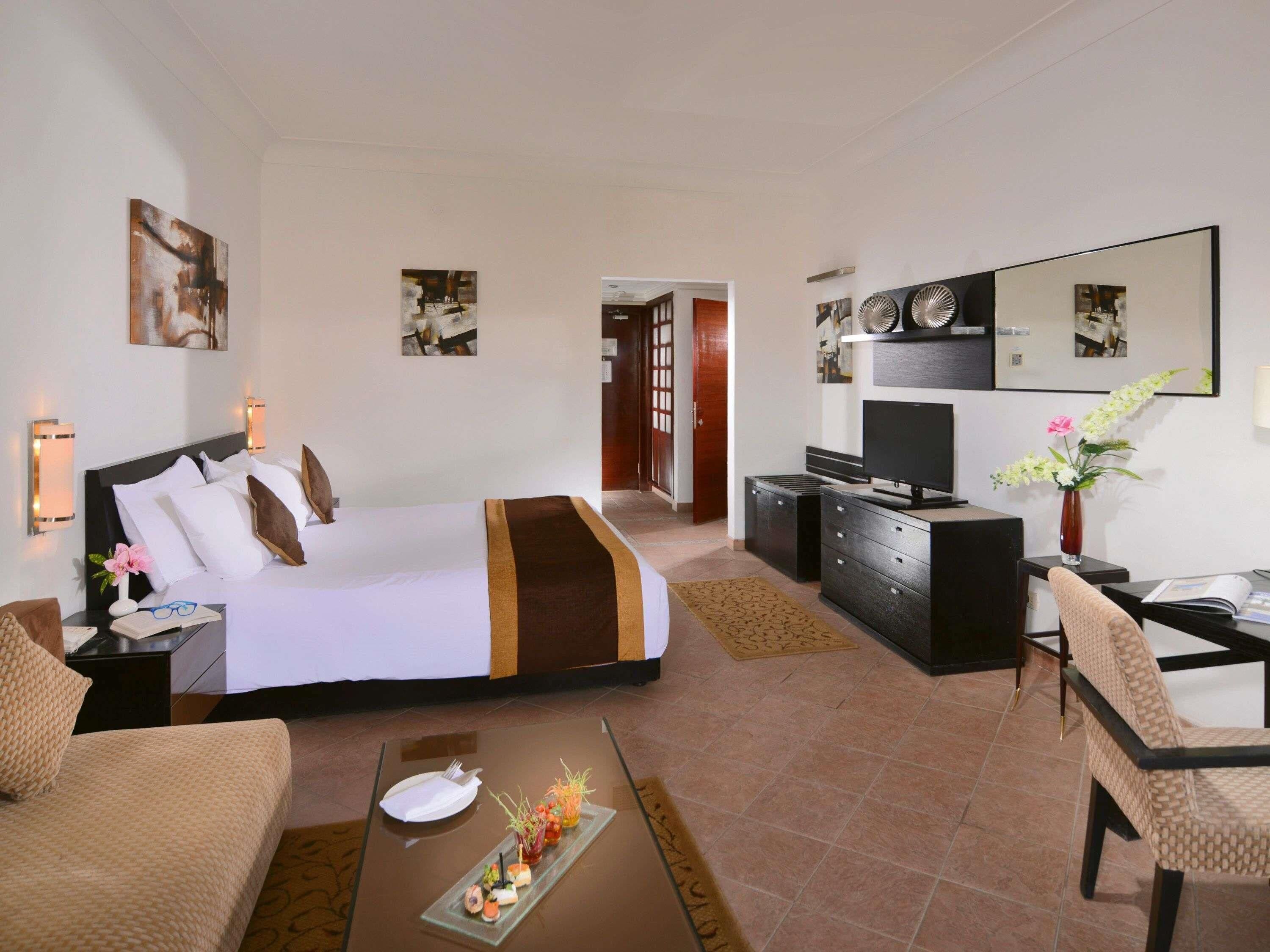 Habitación de hotel con cama, escritorio, televisión, silla y mesa de comedor con una comida ligera.