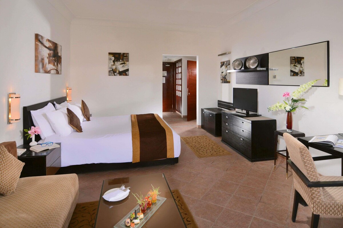 A hotel room with a bed, a desk, a TV, a chair, and a dining table with a small meal.