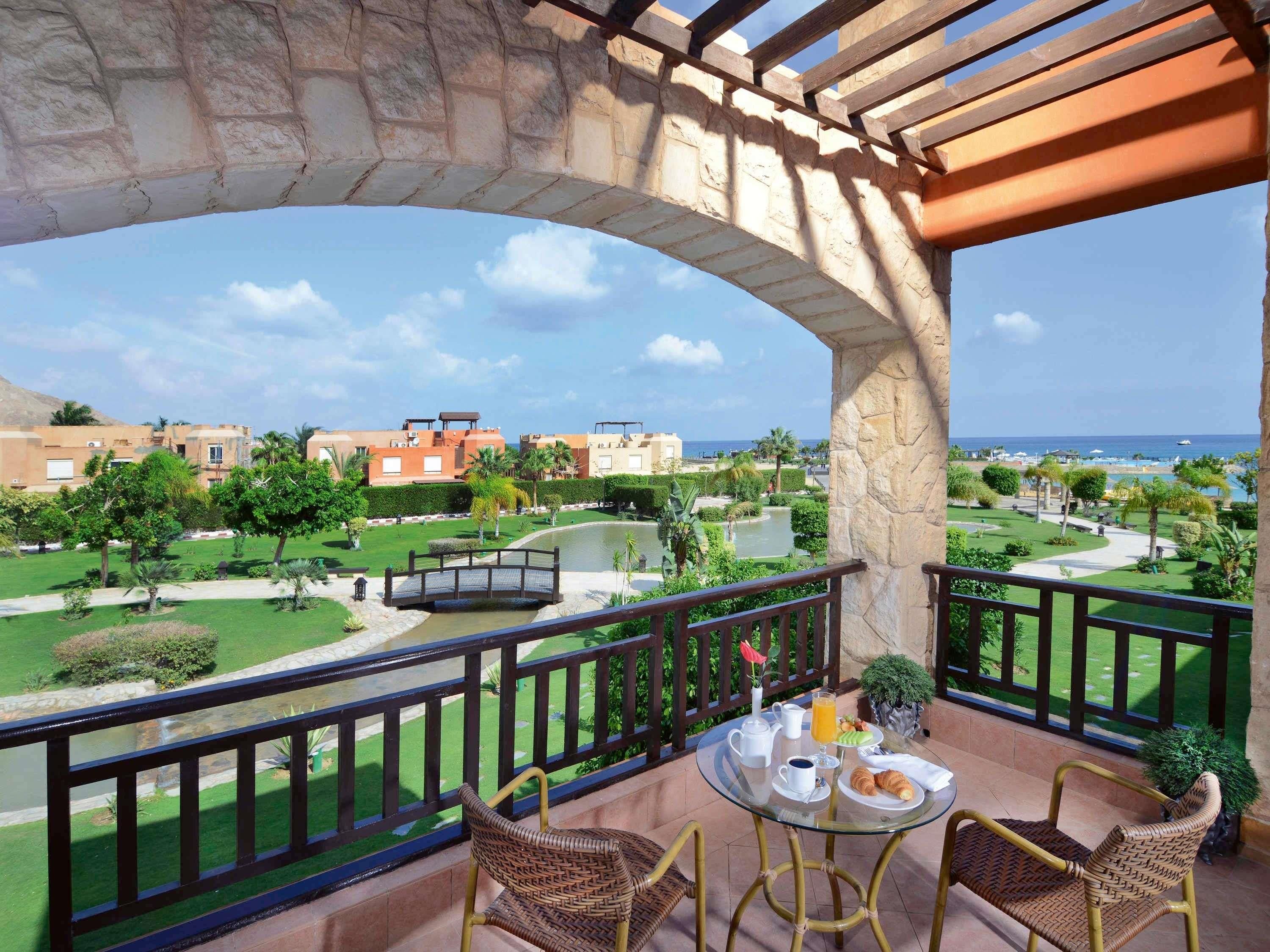 A balcony with a view of a landscaped garden, a pool, and buildings in the background.