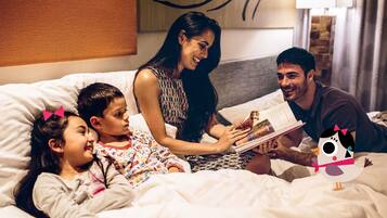 A family in a hotel room with a bed, pillows, and a wall with a decorative pattern.