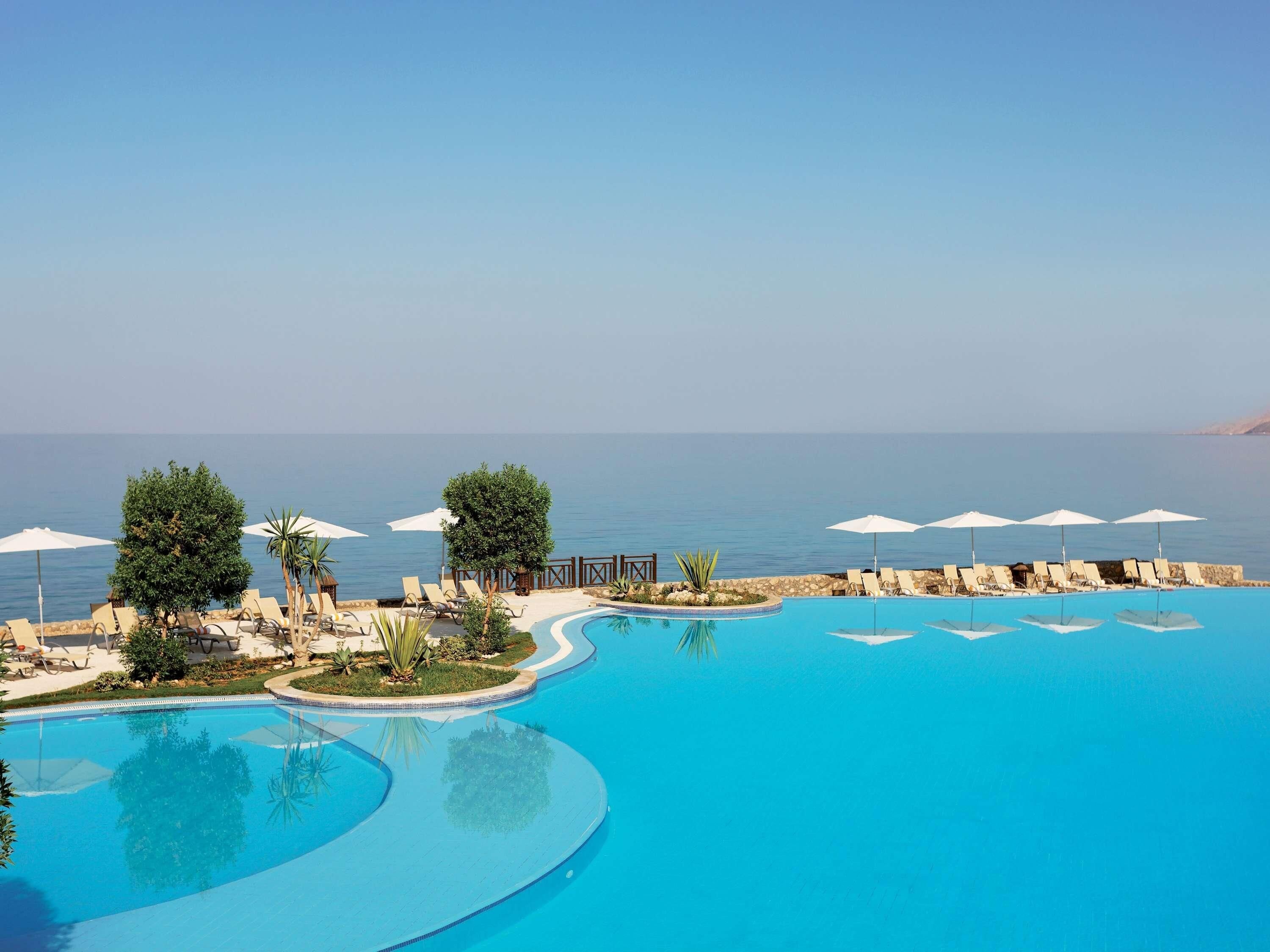 A pool with a view of the sea, surrounded by lounge chairs and umbrellas.
