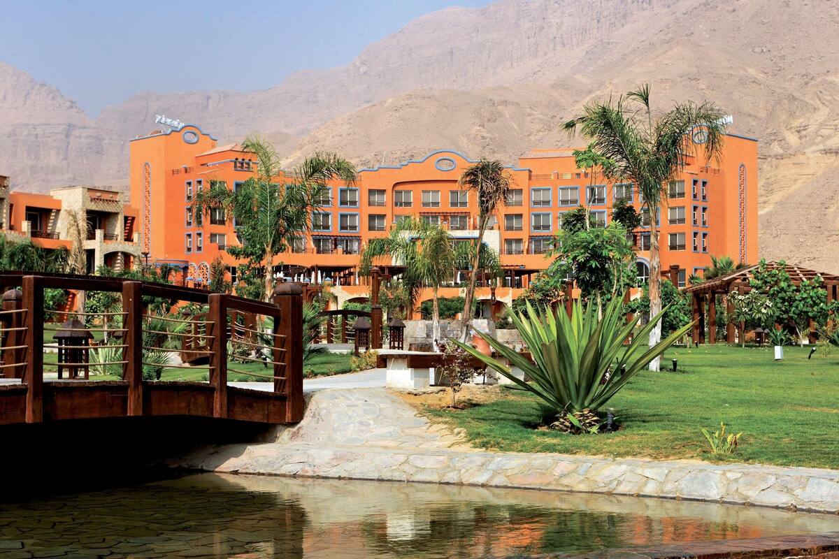 Ein Hotel mit mehreren orangen Gebäuden, einer Brücke und einem Poolbereich mit Steingrenze.