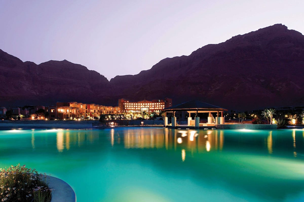 A resort with a pool, a gazebo, and a building with lights against a mountainous backdrop.