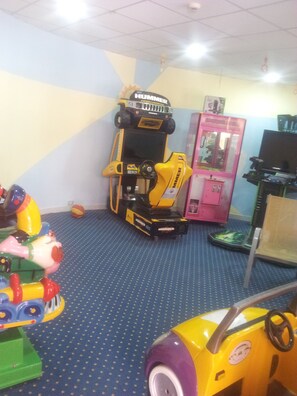 Een speelruimte voor kinderen met een geel en zwart speelgoedvoertuig, een roze grijpmachine en een blauw tapijt.