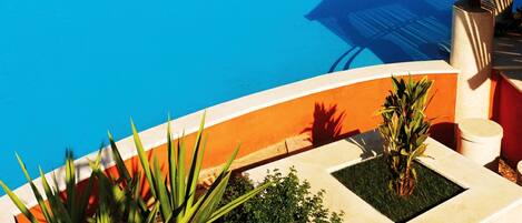 Une grande piscine d’un bleu éclatant, agrémentée de parasols blancs et de chaises longues, entourée de verdure et offrant une vue sur la mer.