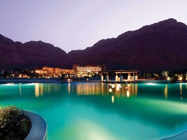 Un resort con piscina, un pabellón y un edificio iluminado frente a montañas.