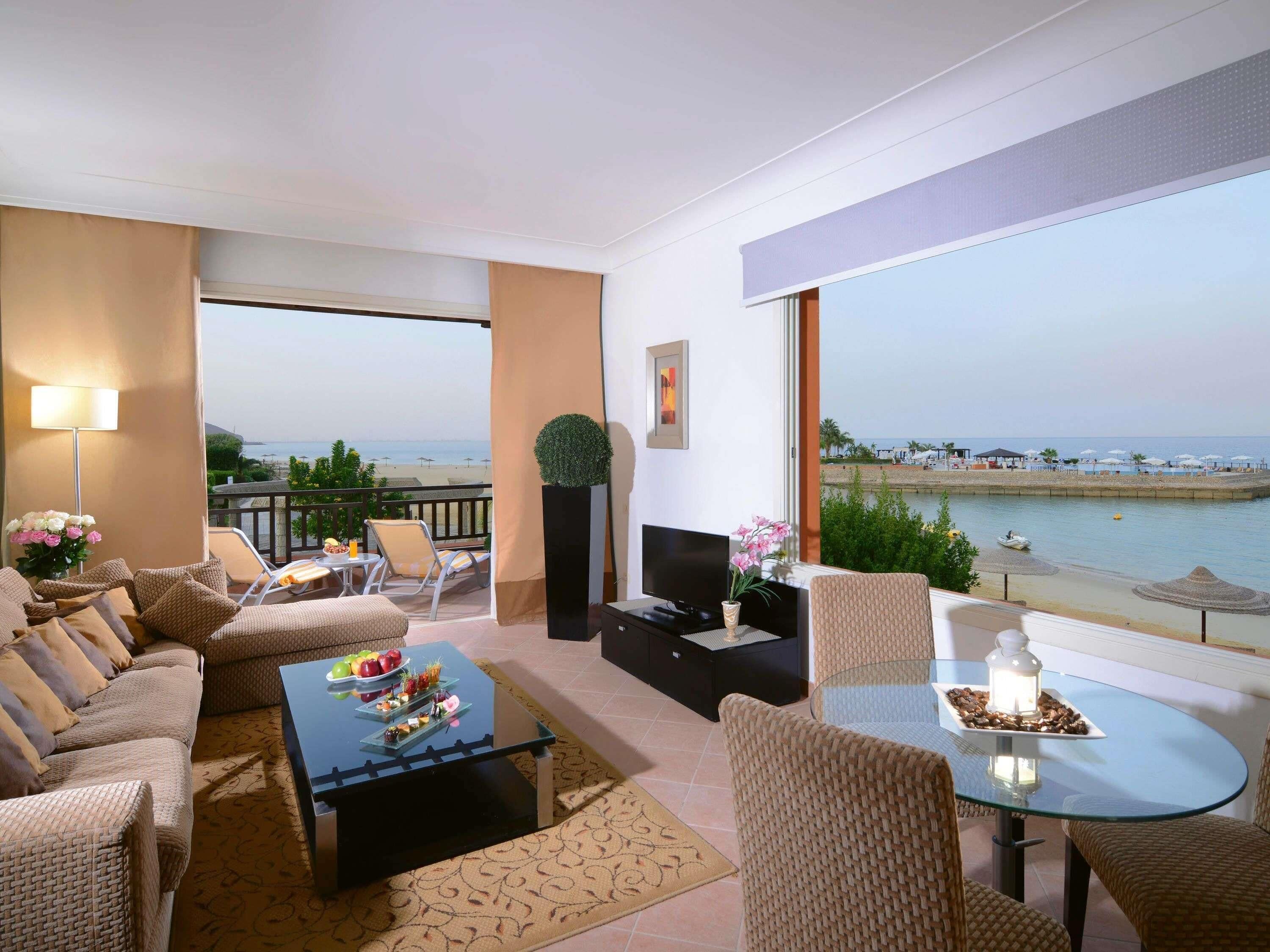 A balcony with a view of the sea, a sofa set, a coffee table with fruit, and a TV.