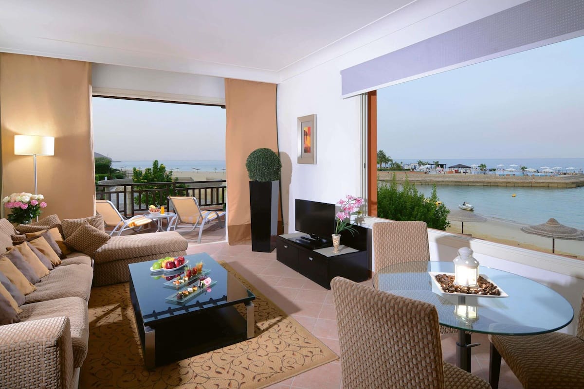 A balcony with a view of the sea, a sofa set, a coffee table with fruit, and a TV.