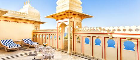 A traditional building with a central tower, a courtyard with lounge chairs and a table, and decorative arches.