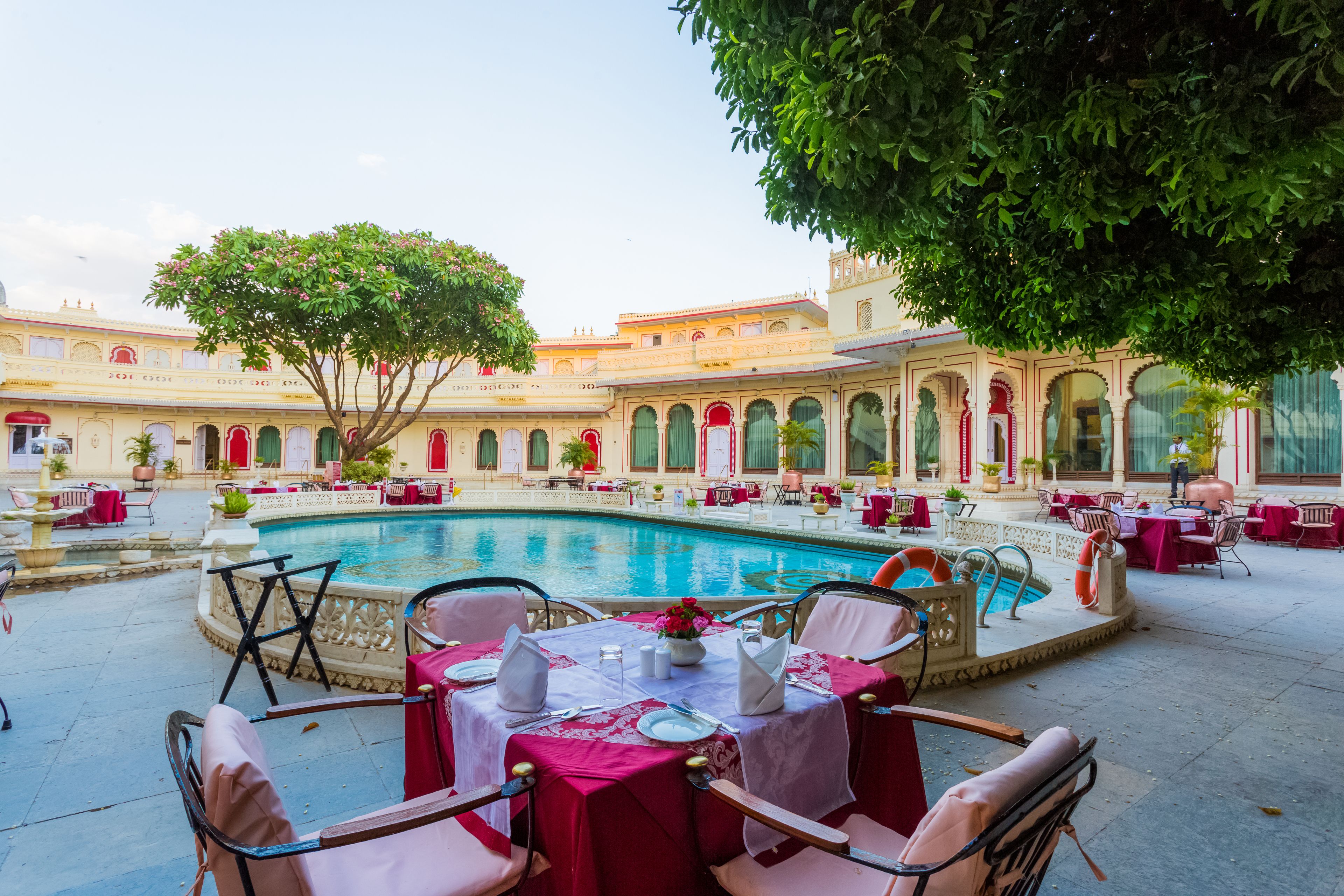 Un patio con piscina, mesas, sillas y un árbol.