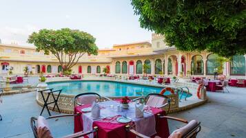 Un patio con piscina, mesas, sillas y un árbol.