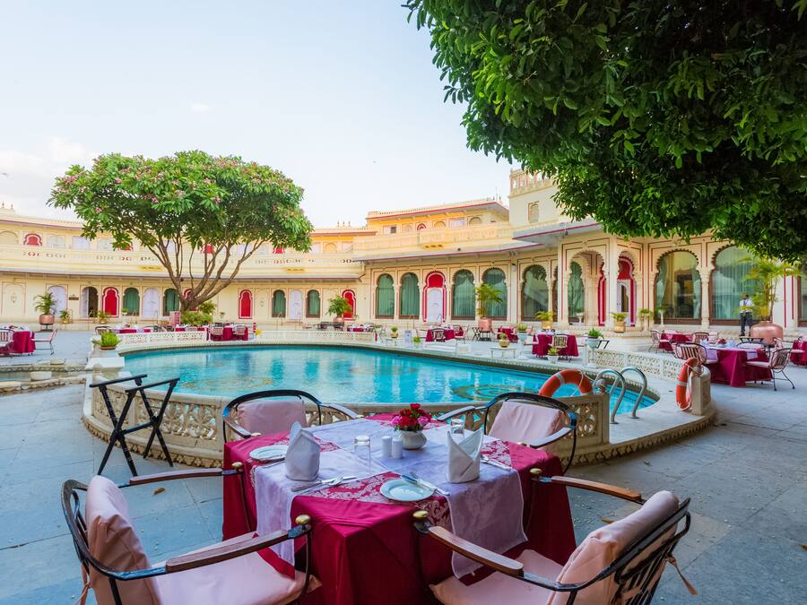 Un patio con piscina, mesas, sillas y un árbol.
