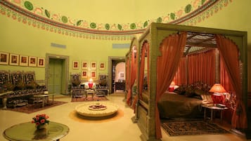 A traditional room with a four-poster bed, a sitting area with sofas, and a dining table.