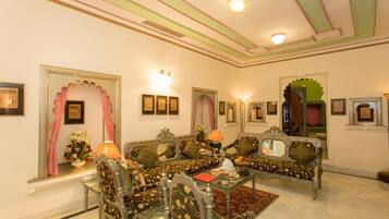 A traditional room with ornate furniture, a glass table, and framed artwork on the walls.