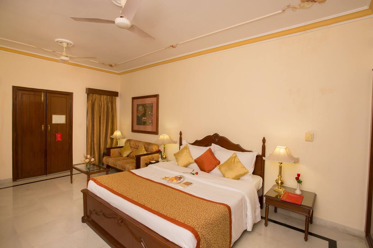 Une chambre d’hôtel avec un grand lit, deux tables de chevet, un ventilateur de plafond, une armoire et un tableau encadré au mur.