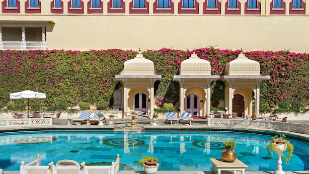 A pool area with a fountain, lounge chairs, and potted plants. - Shiv Niwas Palace by HRH Group of Hotels (Udaipur)