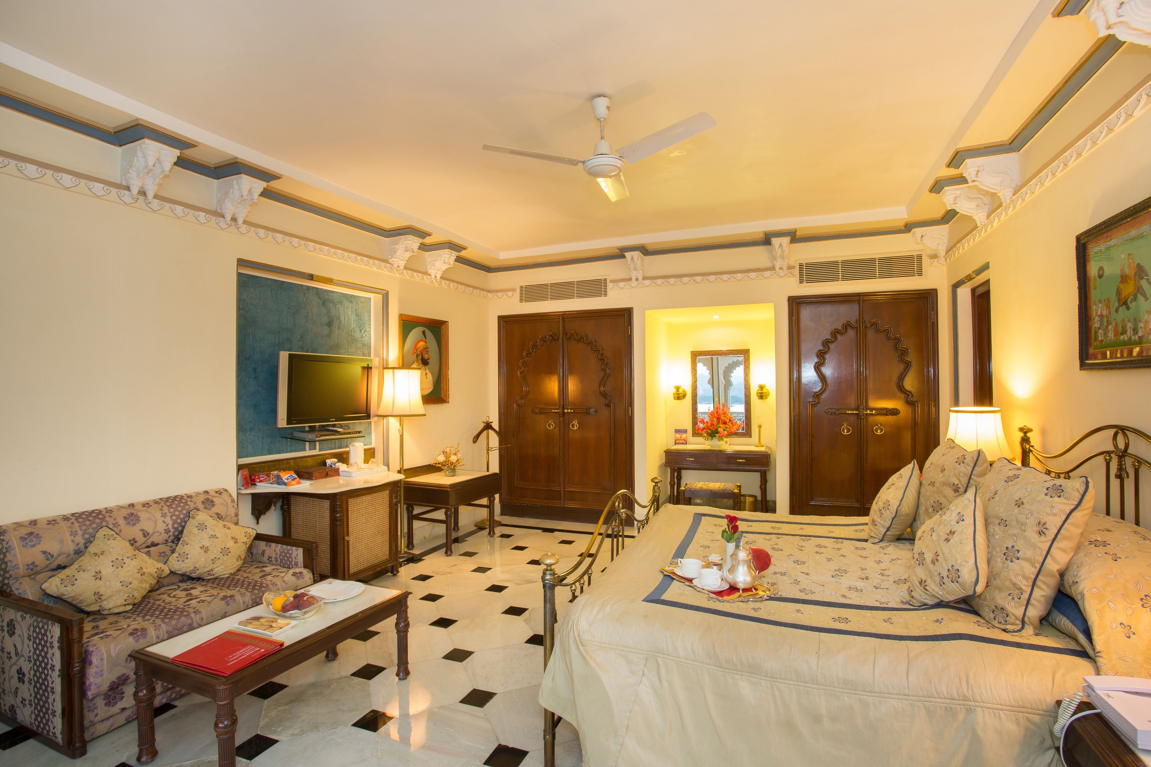 A hotel room with a bed, a sofa, a desk, a television, and a ceiling fan.