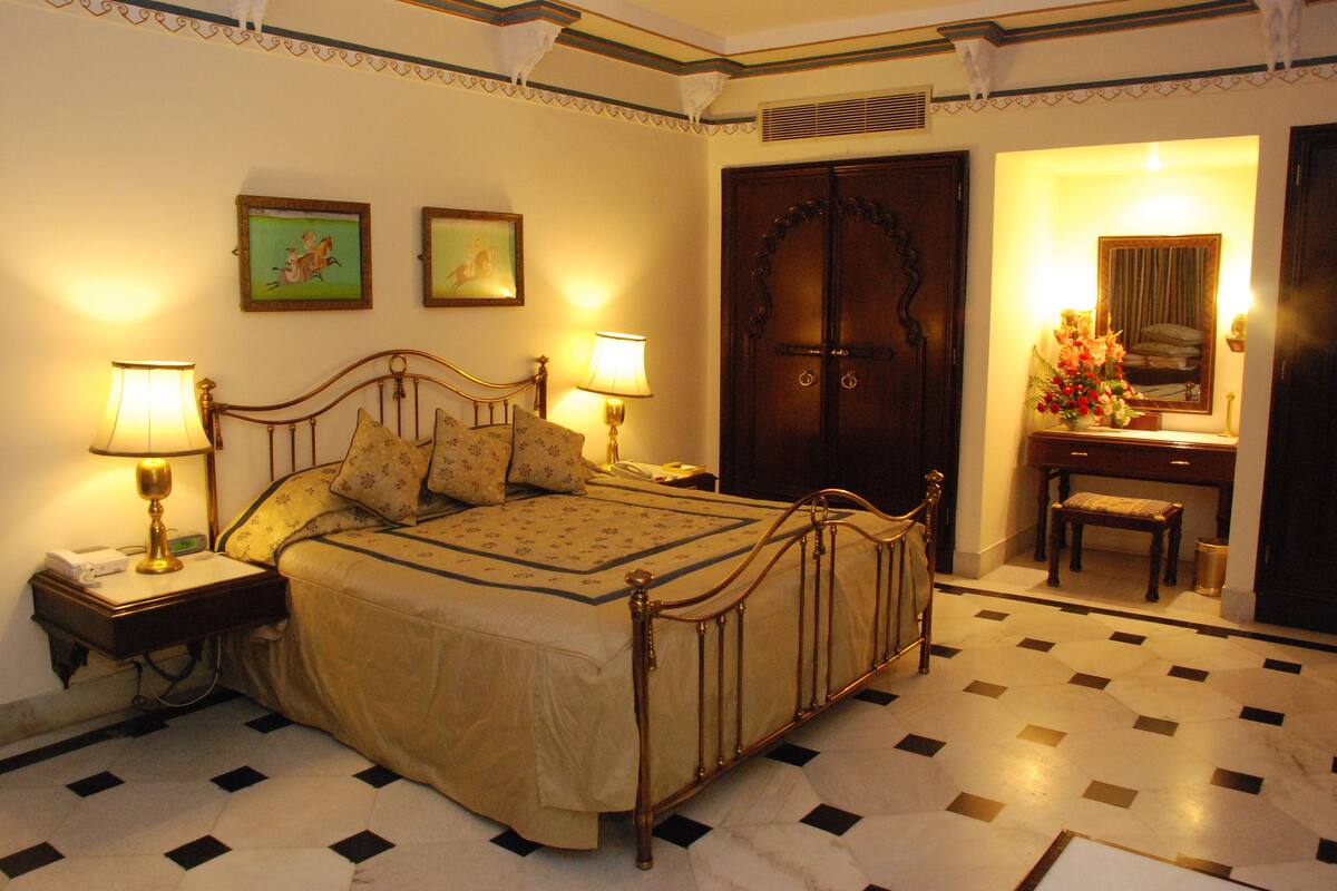 Une chambre à coucher bien rangée, avec un lit, deux tables de chevet dotées de lampes, une commode, un miroir et une porte.