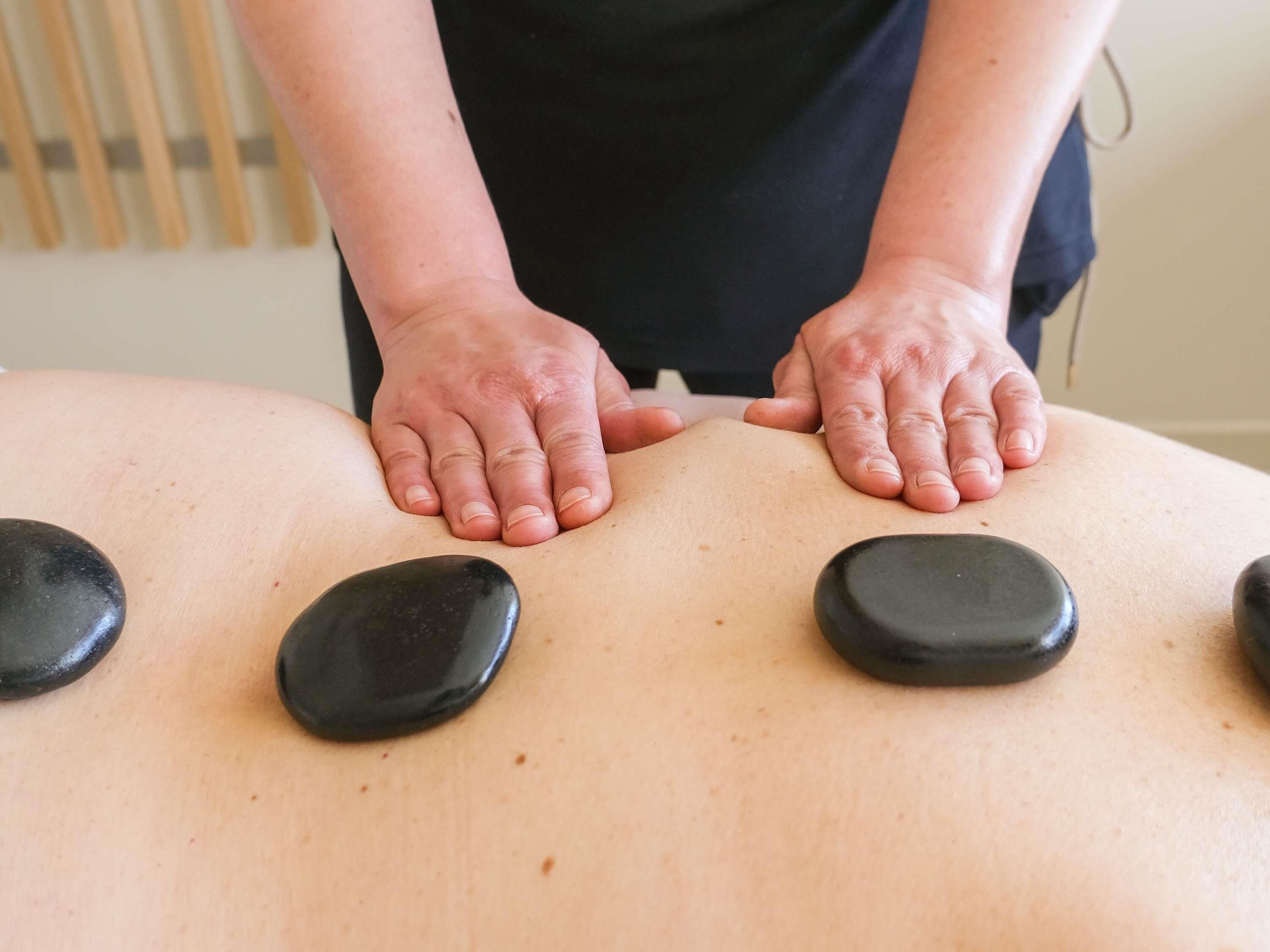 Une personne effectue un massage des pieds sur une table de massage, en utilisant des pierres noires.
