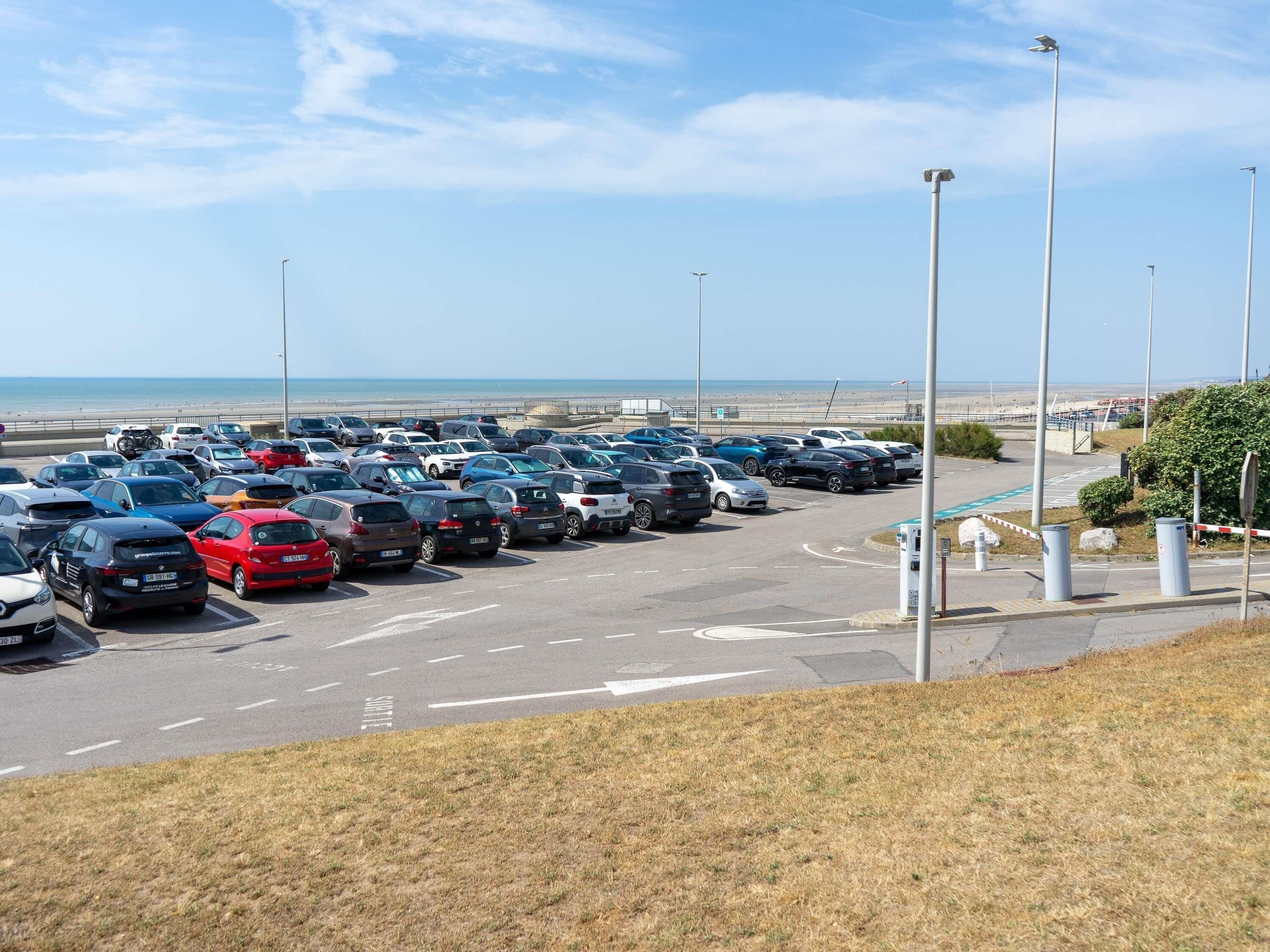 A parking lot with multiple cars and a view of the beach in the background.
