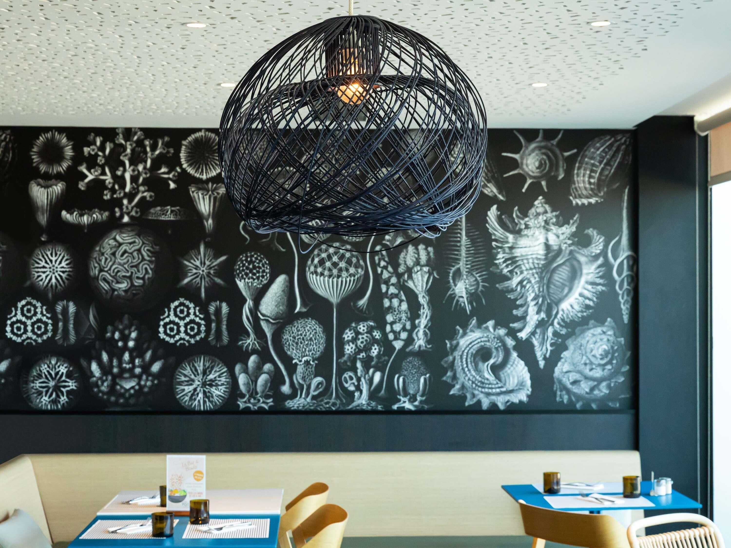 Un comedor con pared de diseño blanco y negro, una lámpara negra esférica colgante y una mesa dispuesta con carta, vasos y cubiertos.