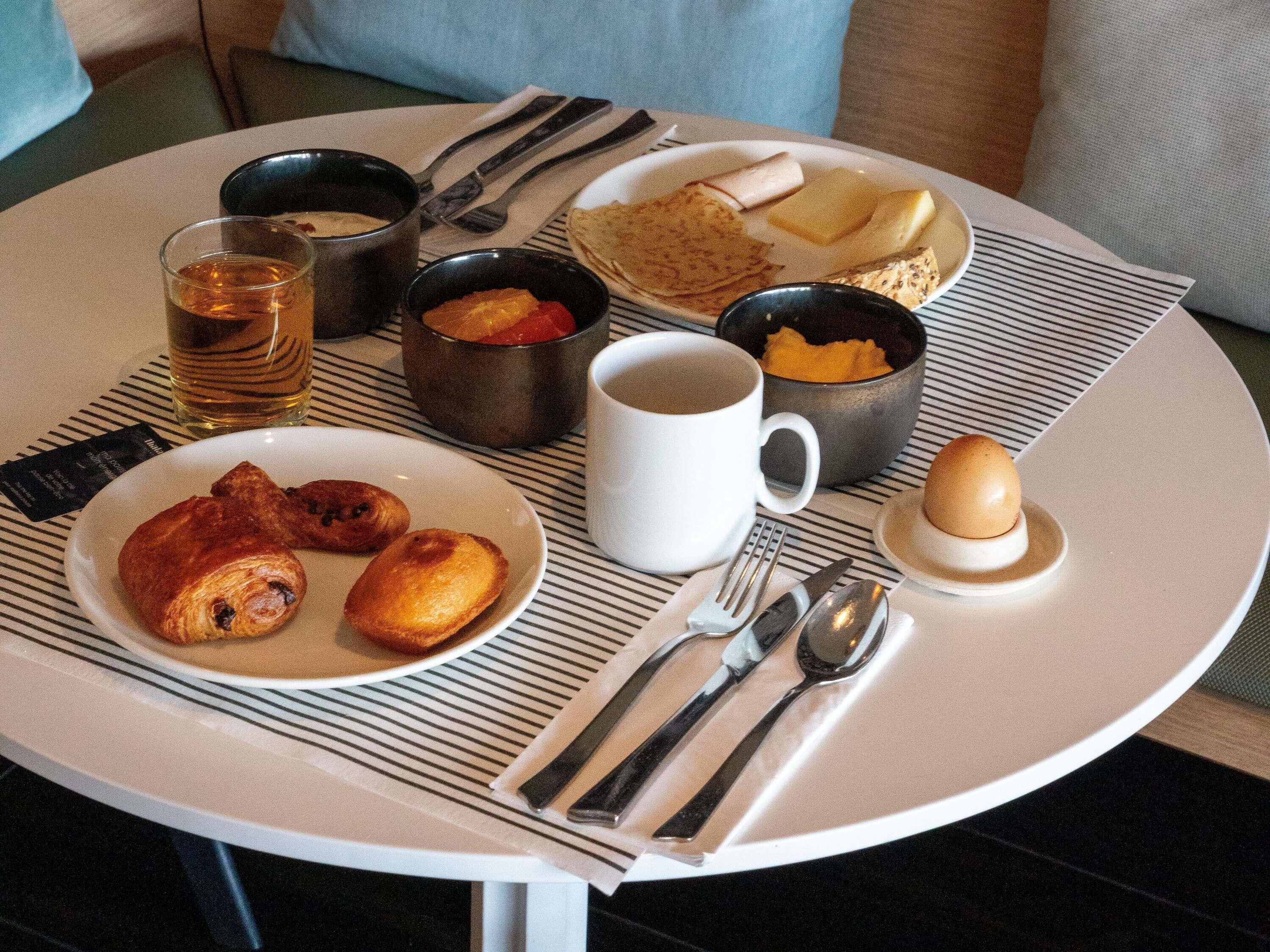 Una escena de desayuno con un plato de pasteles, una taza de café y varios condimentos sobre una mesa redonda.