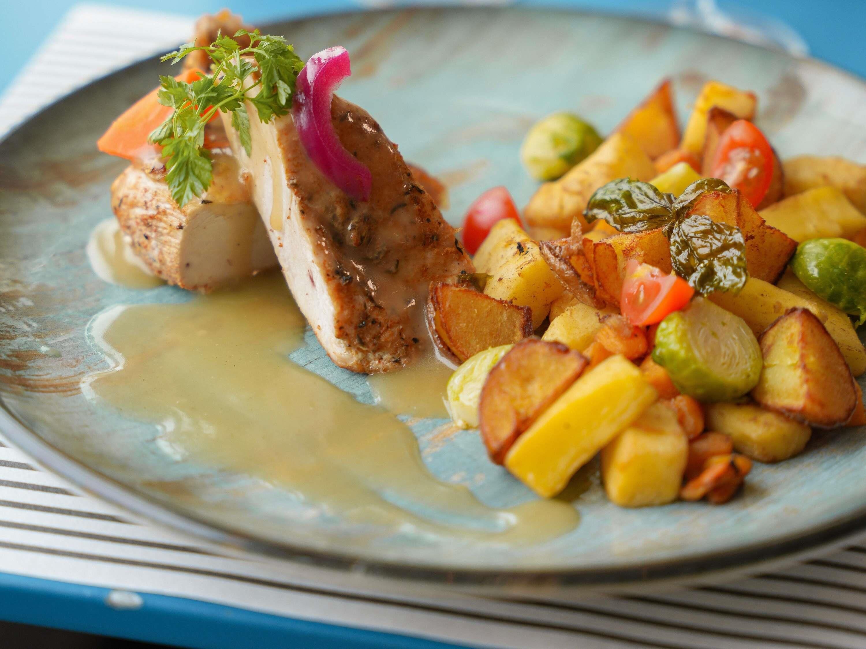 A plate of food with a variety of vegetables and a piece of meat, possibly chicken, with a sauce.